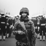 A soldier stands in focus during a military parade in monochrome.